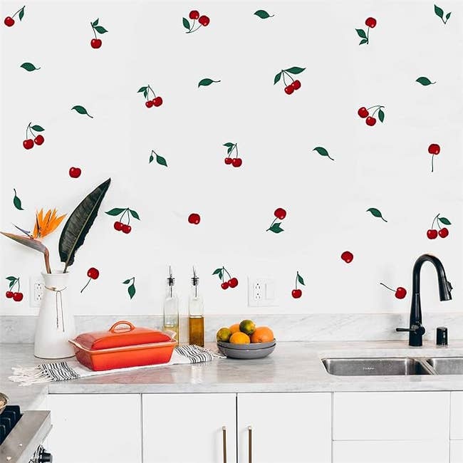 A kitchen with fruit-themed wallpaper, cookware on the counter, and a sink