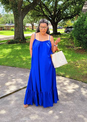 Person successful a flowing summertime formal holds a beige tote bag, lasting connected a driveway.