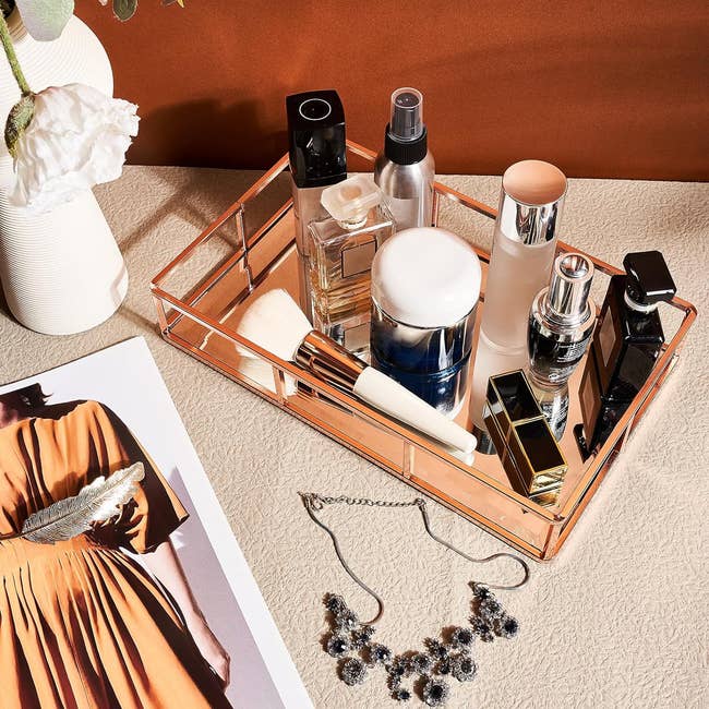 Cosmetic products and accessories arranged on a rose gold mirrored tray 