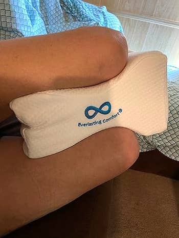 Legs resting with a achromatic genu pillow featuring a bluish infinity logo and