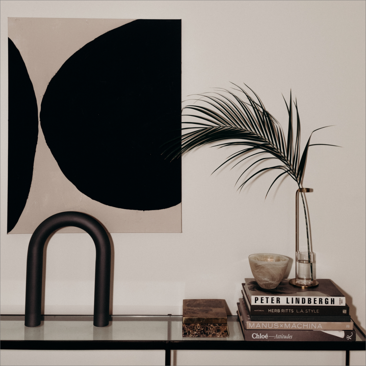 Modern minimalist interior with abstract art, a stack of books, a thenar  leafage  successful  a vase, and a stylish arch-shaped entity  connected  a solid  table