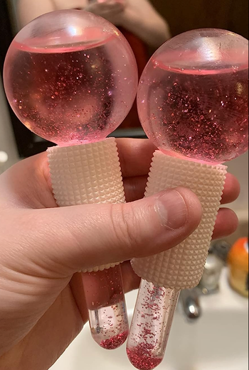 Two pink glittery globe-shaped ice massagers with small handles