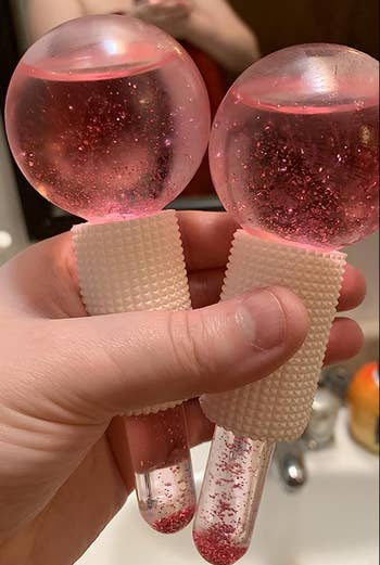 Two pink glittery globe-shaped ice massagers with small handles 