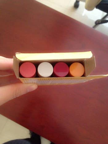 Different reviewer holding up four different flavors of the balm, so that only the different colored tops are shown