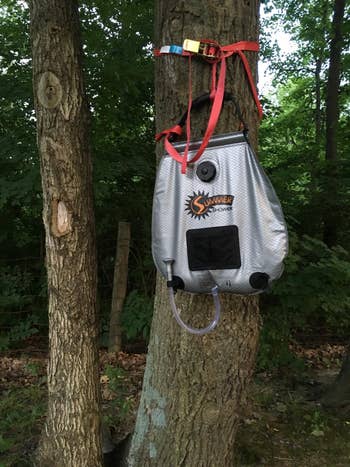 reviewer photo of the portable shower hanging from a tree