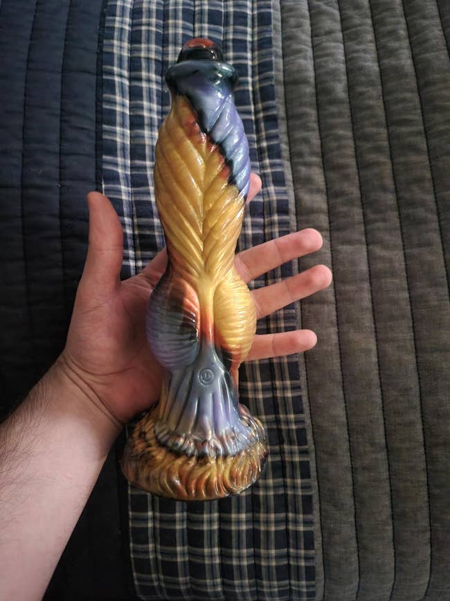 A manus holds a large, intricately designed dildo