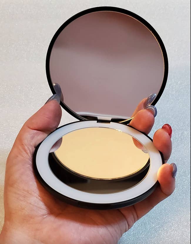 Reviewer holding a small round compact mirror with a light around the edges 