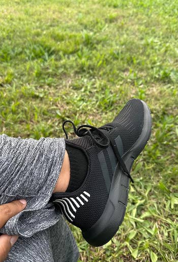 Person's foot wearing a sporty black sneaker, resting on grass, possibly for a shoe feature in a shopping article