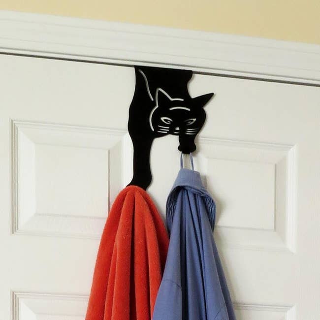 Black cat over-the-door hanger holding up a red towel and a blue shirt