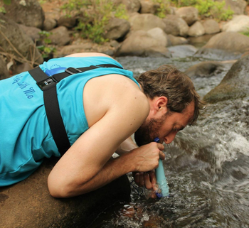 reviewer drinking straight from a river using the blue lifestraw