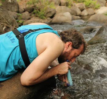 reviewer drinking straight from a river using the blue lifestraw