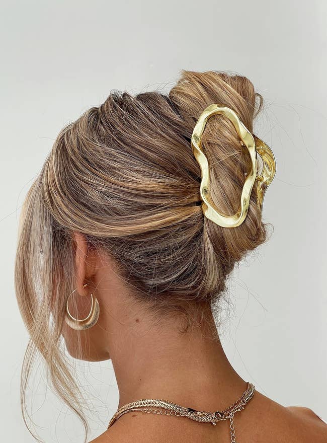 Gold hairsbreadth  clip secures an updo adorned with wavy highlights. Gold hoop earring and concatenation  necklace implicit   the look