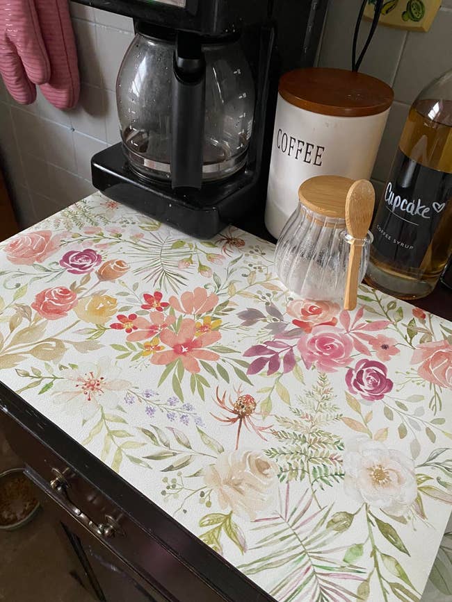 reviewer's floral-patterned dish drying mat next to coffee supplies