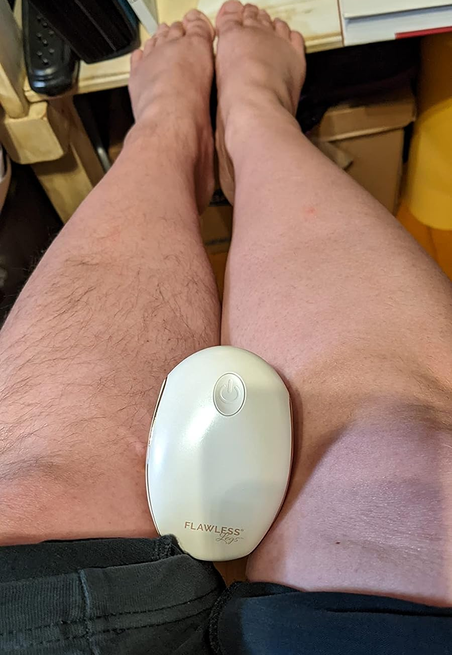 a reviewer with the shaver in their lap with one hairless leg and one hairy leg