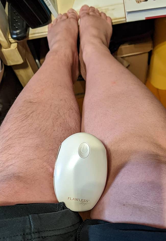 a reviewer with the shaver in their lap with one hairless leg and one hairy leg