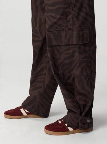 Person wearing zebra-patterned cargo pants and reddish  sneakers with achromatic  stripes, showcasing a casual streetwear style