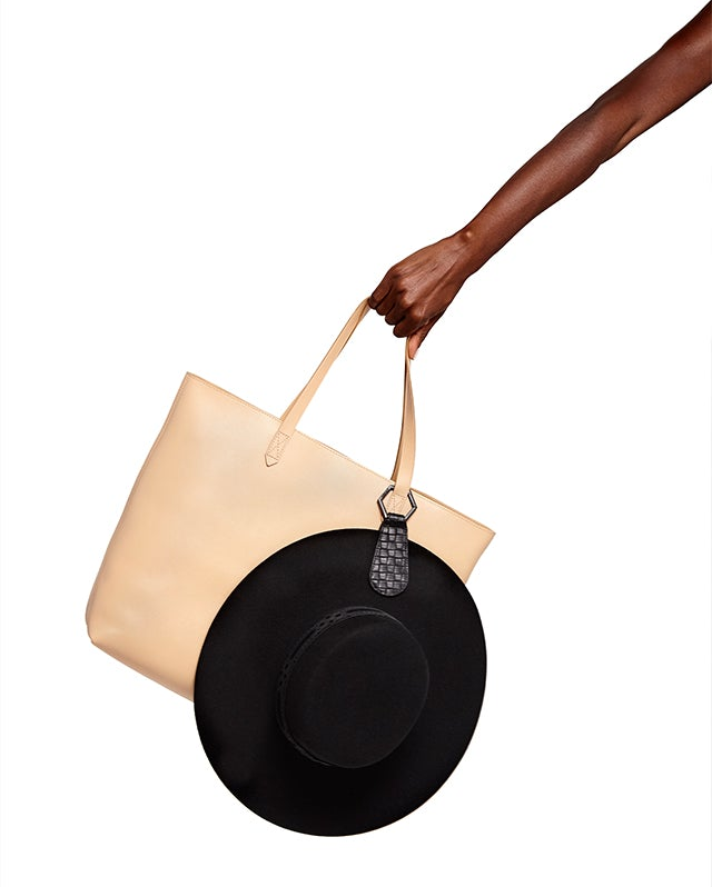 Model holding cream purse with black hat clipped on purse