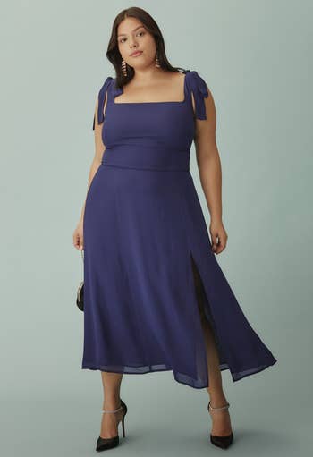 model in a stylish blue dress with ribbon-tied shoulders and a mid-length hem, paired with black heels