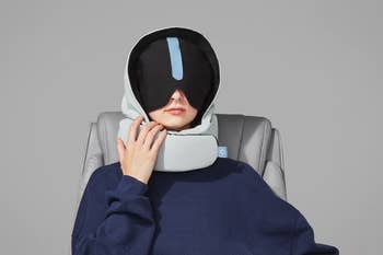 Person seated, wearing a futuristic head and neck massage device, covering eyes, with relaxed posture