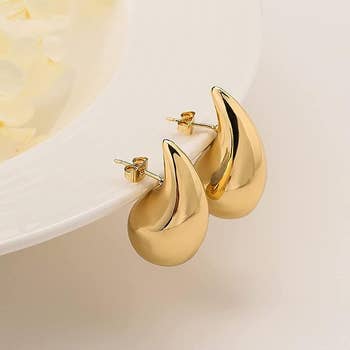 The pair of gold earrings placed on a whie plate