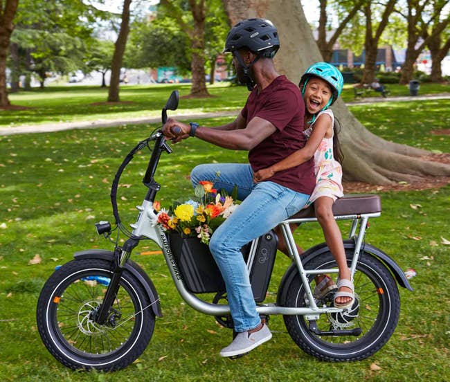 A person is on the electric bike with a child sitting behind them on the passenger seat
