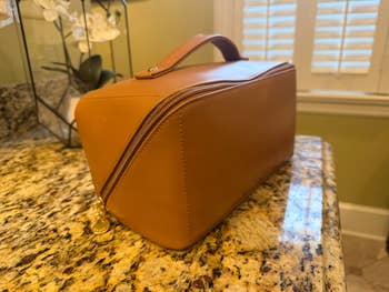 Rectangular leather toiletry bag with handle on granite counter, next to window and orchid plant