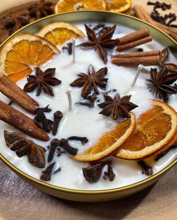Decorative candle topped with dried orangish  slices, cinnamon sticks, prima  anise, and cloves