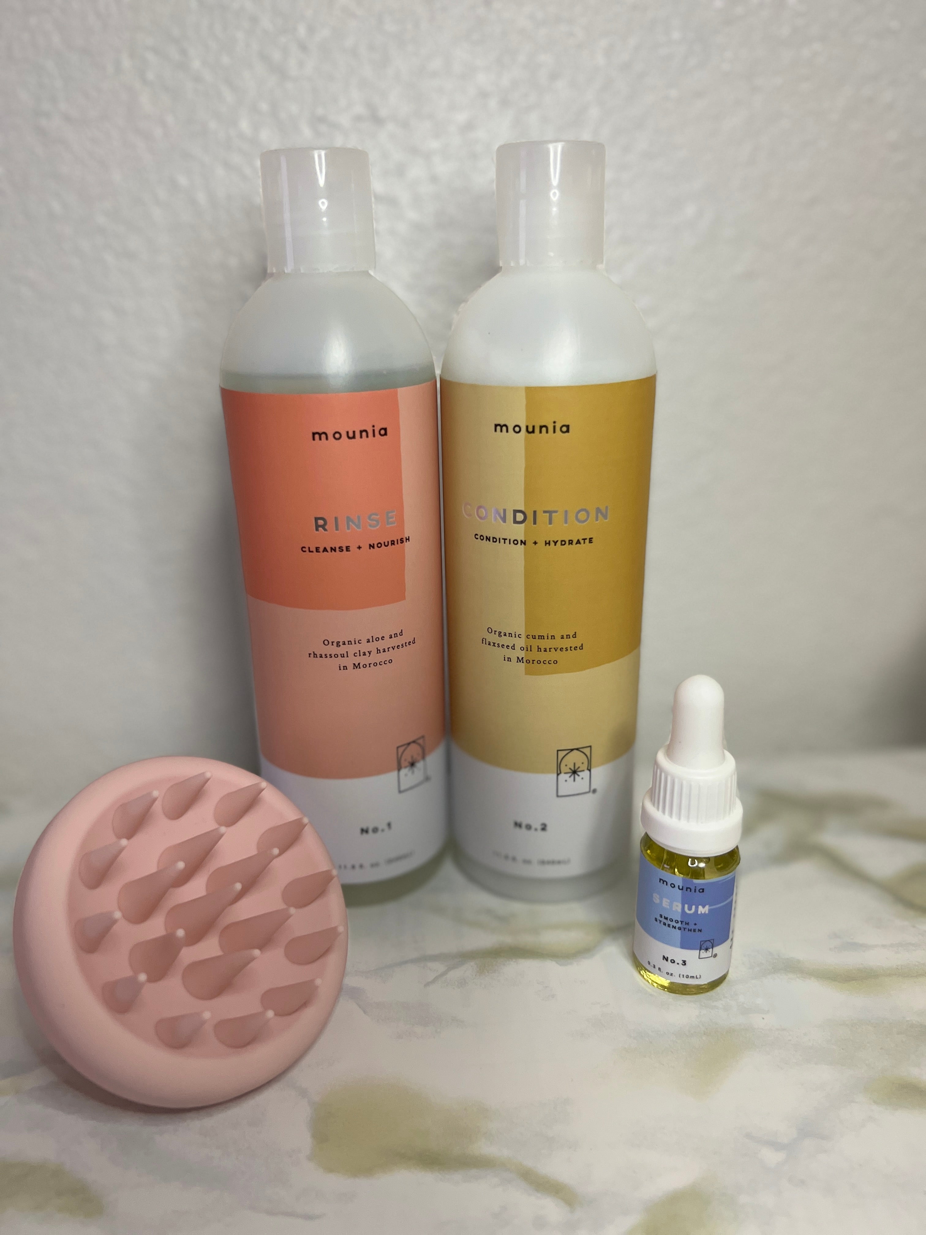 the bottled shampoo and conditioner set next to pink scalp massager on tile