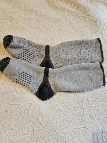 Two grey  socks with achromatic  bottommost   and toed  accents, lying connected  a textured surface