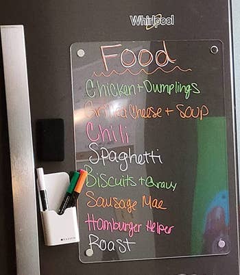 A clear rectangular dry erase board hung vertically on a fridge with an ingredients list 