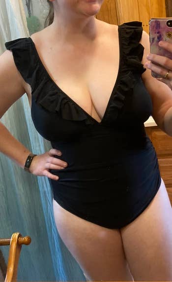 Woman taking a mirror selfie while wearing a black swimsuit with ruffle details