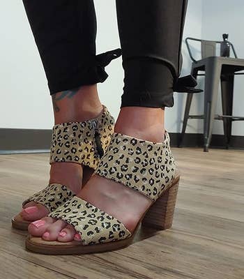 a reviewer wearing a pair of open-toed, cheetah-print sandals with a block heel 