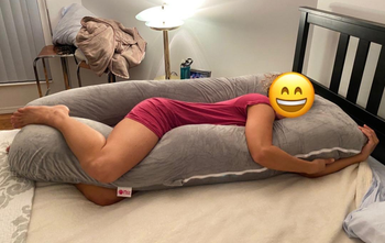 Reviewer laying on light gray U-shaped pregnancy pillow