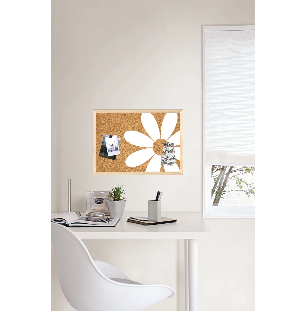 Modern white desk with chair, corkboard featuring a daisy design, and various office supplies by a window with sheer blinds