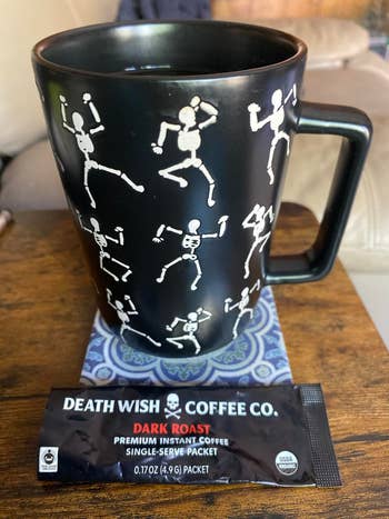 reviewer's mug decorated with skeletons adjacent  to an opened packet of coffee