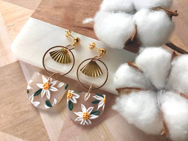 The earrings have a gold fan inside a ring and under that is a white frosted clay semi circle with white florals sculpted on