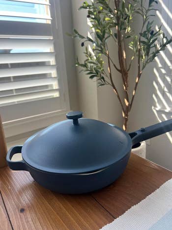 A blue saucepan with a lid on a wooden table next to a potted tree