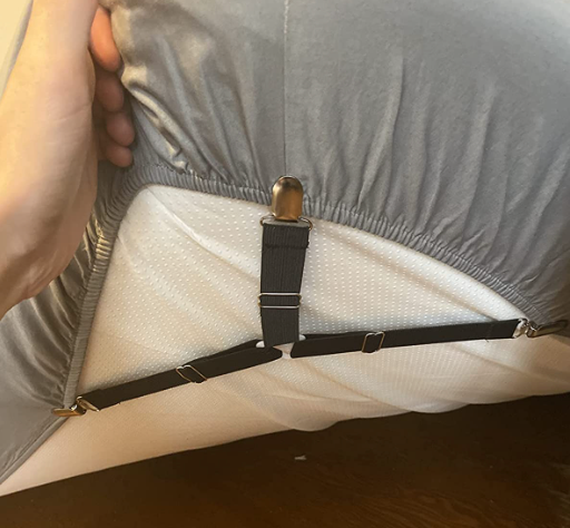 A reviewer's hand holding up the corner of a mattress showing the fastener holding the sheet in place