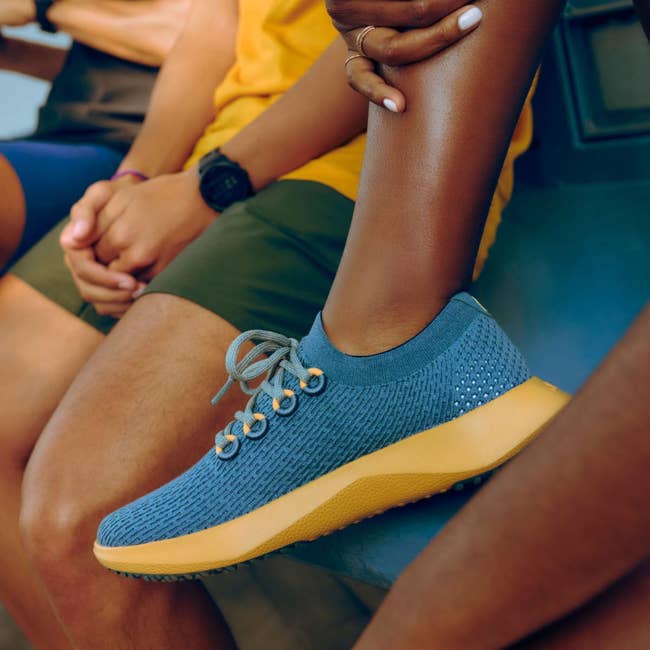 a model wearing a blue and yellow tree dasher 2 sneaker