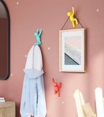 three colorful Buddy wall hooks holding various things, like a jacket and a picture frame