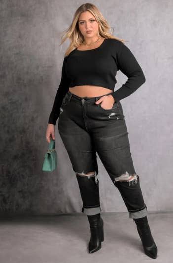a model wearing the crop top in black paired with ripped jeans, heeled boots, and a handbag 