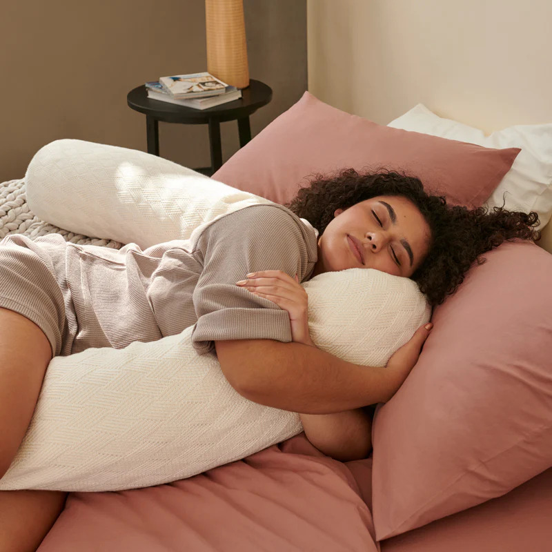 model holding the pillow between her arms and legs with extra length behind her back as support