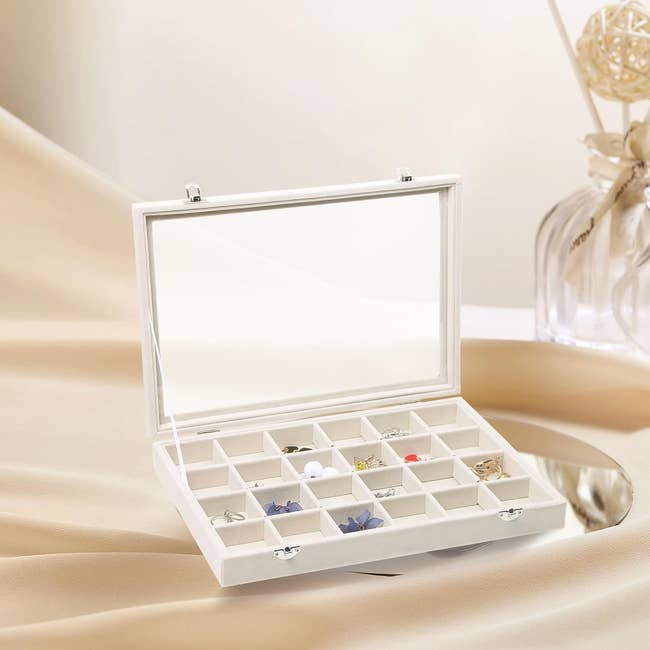 Jewelry container  with aggregate  compartments containing assorted  jewelry items sits unfastened  connected  a mirrored surface. Decor portion   with sticks successful  solid  jar successful  the background