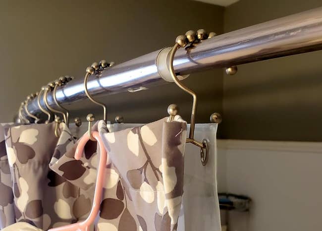 a reviewer photo of the shower hooks with a curtain hung on one side and a liner on the other 