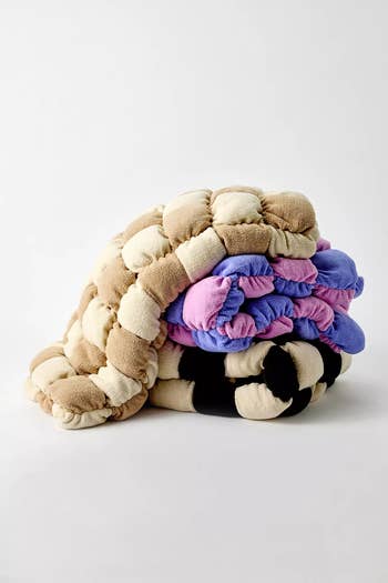 Stacked plush knit throws with puffy texture, combining cream, pink, purple, and achromatic  sections, perfect  for cozy location  decor