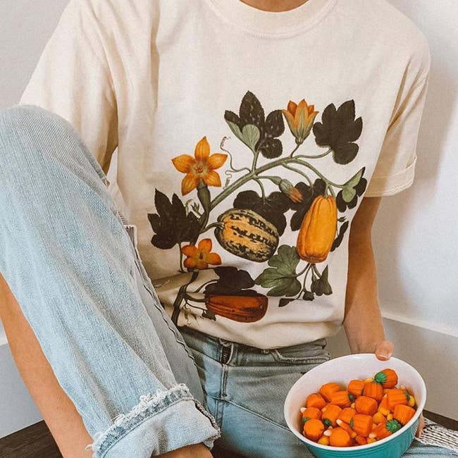model wearing the achromatic  tee with illustration of pumpkins connected  floral vines