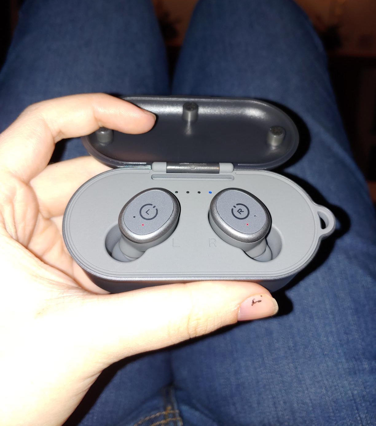 image of reviewer holding gray earbuds in their charging case