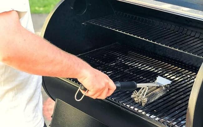 a reviewer using the brush to clean a grill grate 