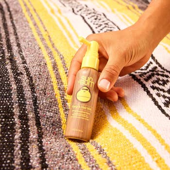 Hand holding Sun Bum Scalp & Hair Mist vessel  connected  a textured surface