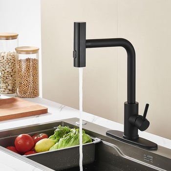 Modern matte black kitchen faucet with water running over fresh vegetables in a sink 